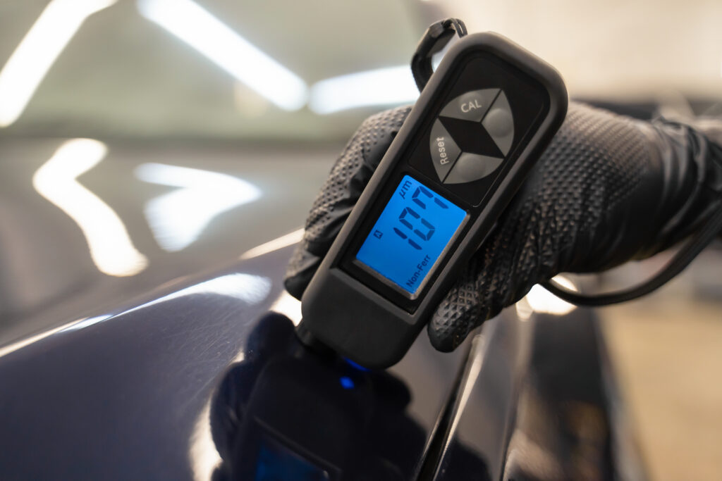 Detailing worker checks the condition of the paintwork with electronic thickness gauge. Car polishing concept